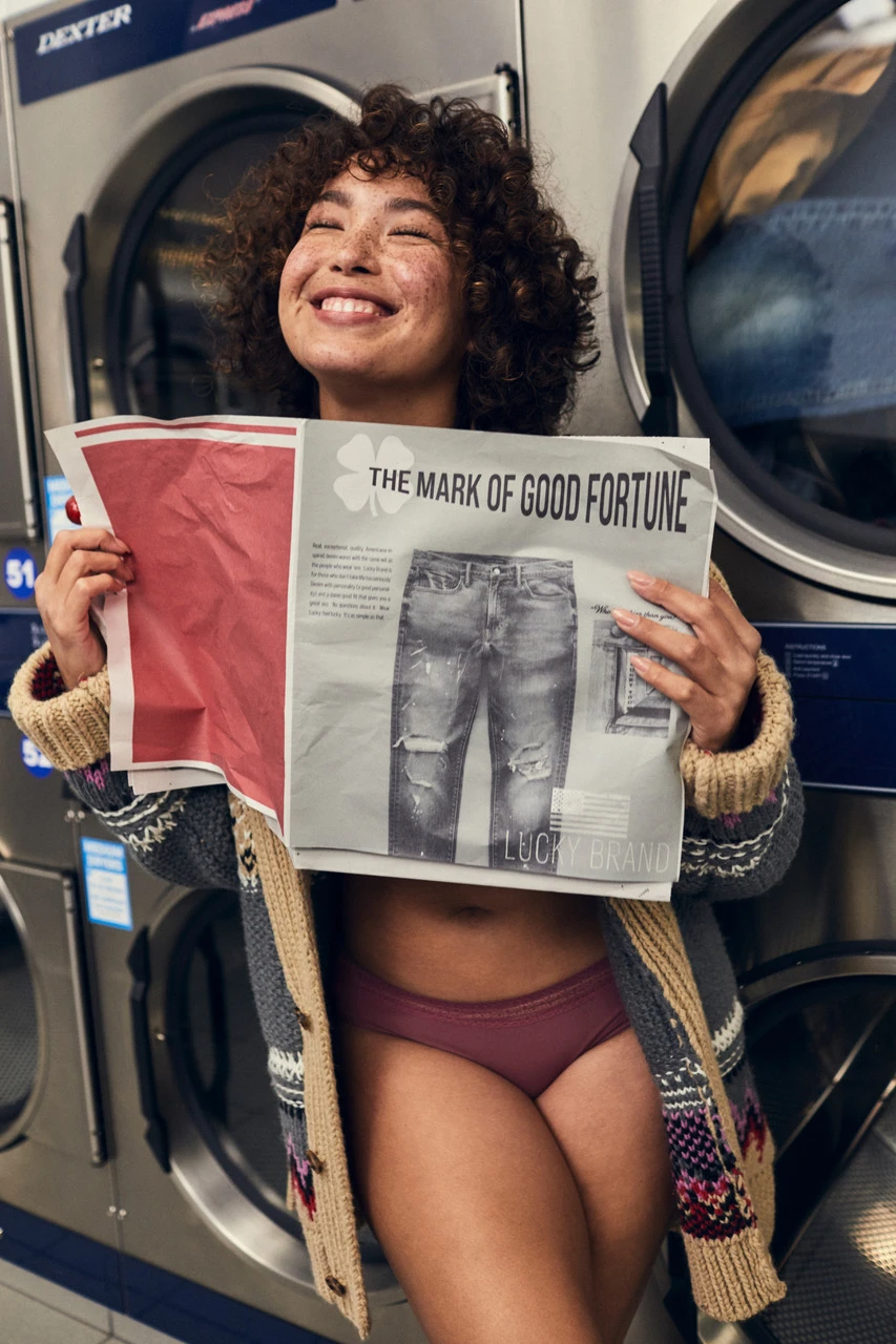 A woman in a laundromat holding up a color tabloid newspaper